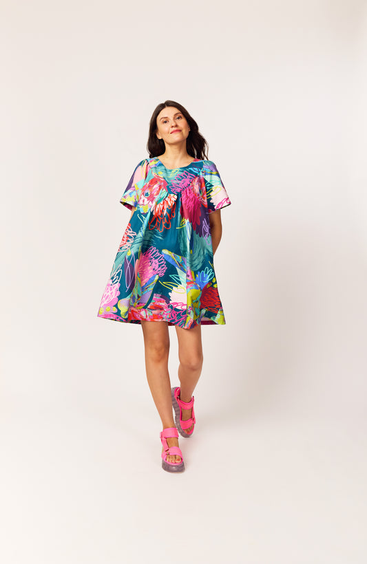 Lanya wearing The Debut Dress in Protea Collage print – bold organic cotton mini with teal base, collage floral pattern design, painterly details and pops of neon.